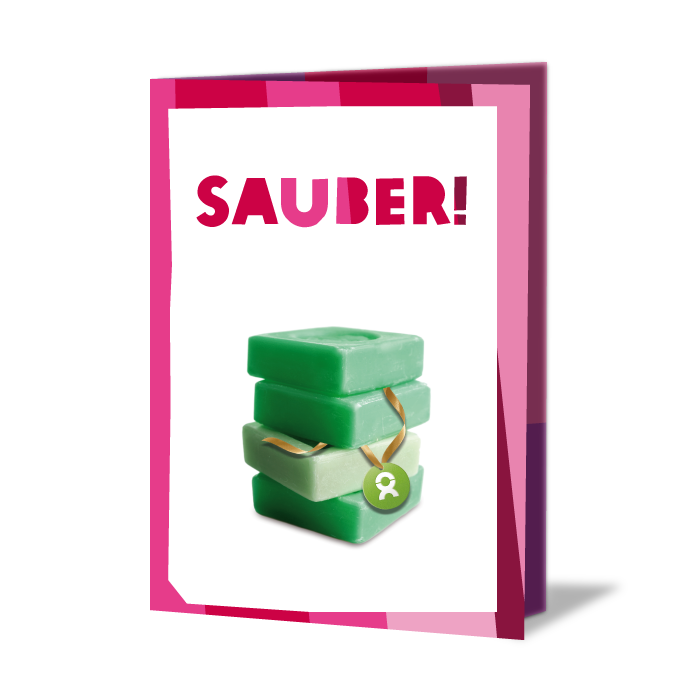 Geschenkkarte mit Aufschrift: Sauber! Darunter ein Stapel grüner Seife
